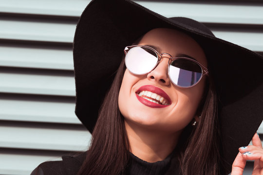 Smiling young model in sunglasses and hat posing at the street. City lifestyle portrait