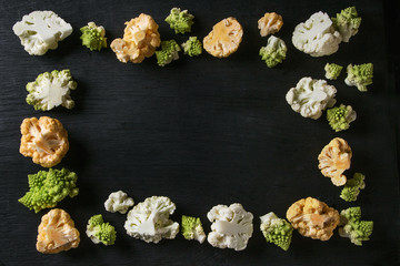Obraz na płótnie Canvas Variety of fresh raw organic colorful cauliflower and cabbage romanesco over black wooden surface. Food frame background. Top view with space. Healthy eating concept