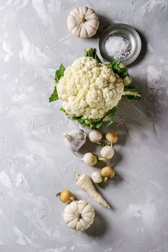 Variety of white vegetables raw organic cauliflower, pumpkins, garlic, parsnip and radish with plate of sea salt over gray texture background. Top view with space. Healthy eating concept