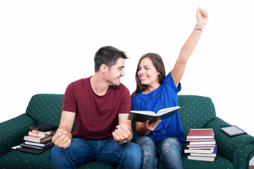 Student couple sitting on couch making victory gesture