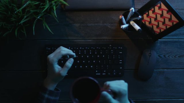 Overhead shot of man drinking coffee and warming up his hands before typing