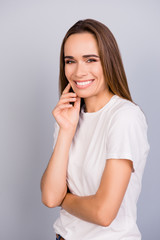Close up portrait of successful young lady in white casual tshirt, standing on the pure light grey background, adorable, charming, looks in camera, with silky straight hair, smooth clean skin