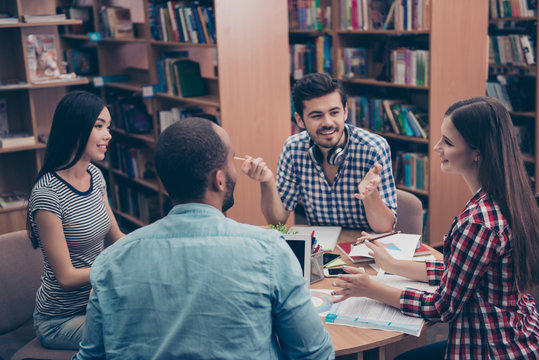 International group of four cheerful clever young students bookworms studying in the ancient university library, sit at the table with books and pdas, speack, share, in casual outfits