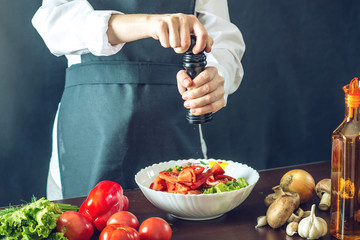 The chef in black apron makes a vegetable salad. Concept of eco-friendly products for cooking