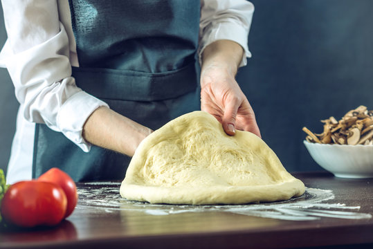 The Chef In Black Apron Makes Pizza Dough With Your Hands On The Table