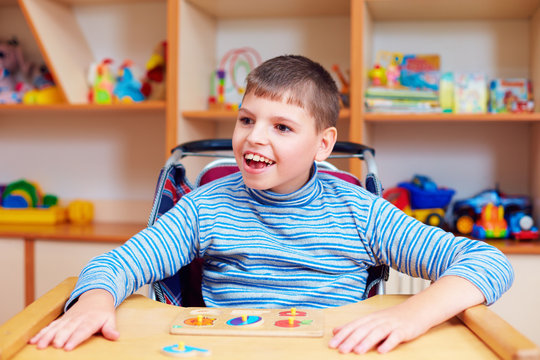 cheerful boy with disability at rehabilitation center for kids with special needs, solving logical puzzle