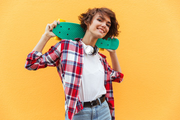 Happy pretty teenage girl holding skateboard on her shoulders