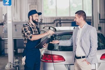 Deal! Side profile shot of cheerful professional repairman in cap and uniform, presenting keys of silver car to classy man owner. Car breakdown, check condition, inspection, engineering, insurance