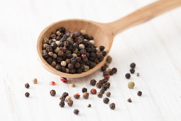 Red, white and black pepper in wooden spoon on white wooden table