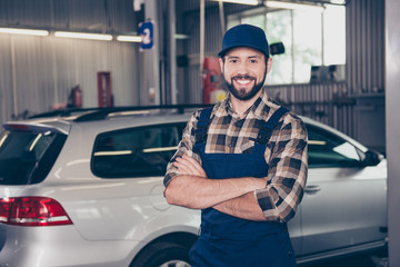 Attractive successful caucasian car expert at work shop standing with arms crossed and smiling at...