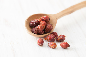 Dried rose hips in wooden spoon on white wooden table