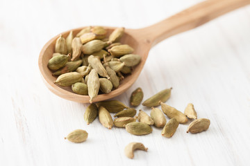Cardamom in wooden spoon on white wooden table