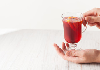 Full glass of mulled wine with slices of orange in the hands