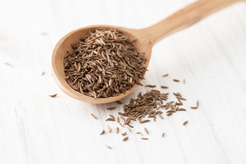 Black cumin in wooden spoon on white wooden table