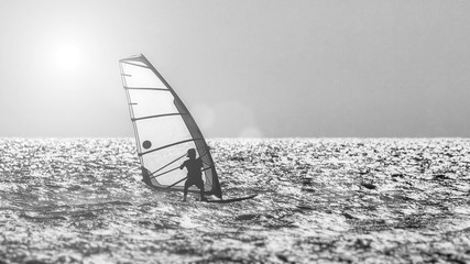 Windsurfer silhouette against a sunset background. Windsurfer Surfing The Wind On Waves, Recreational Water Sports, Extreme Sport Action. Sporting Activity. Healthy Active Lifestyle. Summer Fun