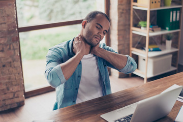Young frustrated afro american freelancer is having a strong pain in neck. He is at home office,...
