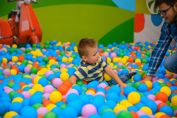 Fototapeta na wymiar A boy with father in the playing room with many little colored balls