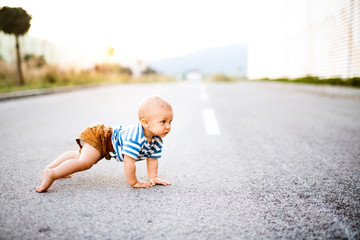 Naklejka premium Little baby boy crawling outside on the road.