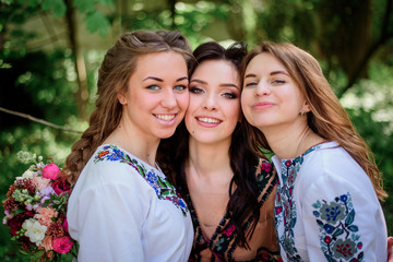 Pretty bride and her bridesmaids in embroidered dresses stand in green park