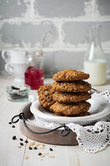 Stack of oatmeal cookies with chocolate on a light background with flakes and a bottle of milk. Selective focus.