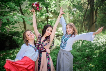 Fototapeta premium Pretty bride and her bridesmaids in embroidered dresses stand in green park