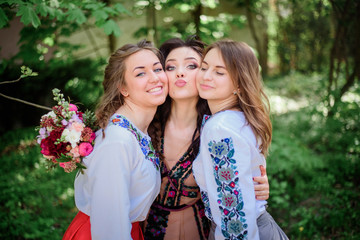 Pretty bride and her bridesmaids in embroidered dresses stand in green park