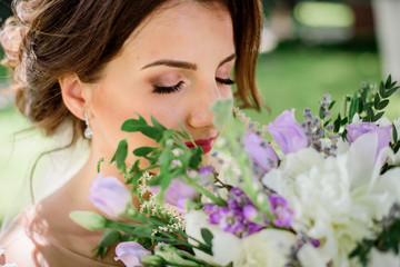 Fototapeta premium Dreamy bride holds violet bouquet before her face
