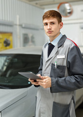 Portrait of a car mechanic in a car workshop, in the background of dealership