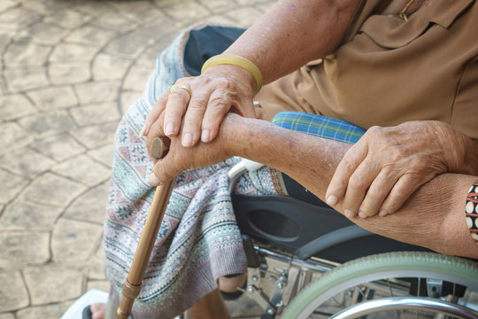 old man take care old lady sit in wheelchair and hold in hand together