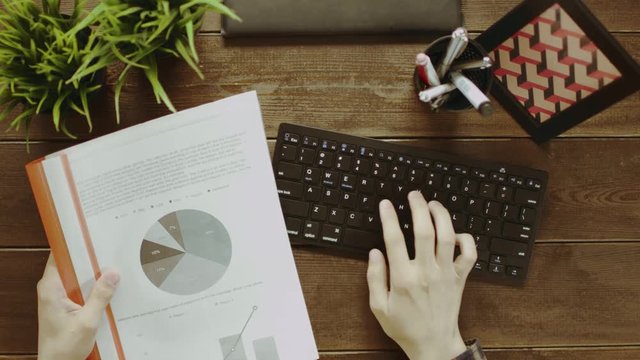Top dowm shot of man entering data of diagrams and graphs on his keyboard