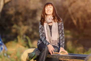 red-haired woman sitting on bench in park with book and laughing