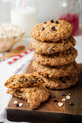 Stack of oatmeal cookies with chocolate on a light background with flakes and a bottle of milk. Selective focus.