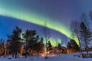 Foto auf Alu-Dibond Grüne Nordlichtgürtel in einem blauen Himmel über einem Häuschen im Lapplandwald © Simone