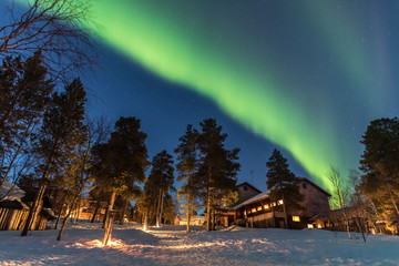 Green Northern lights belts in a blue sky over a cottage in the lapland forest