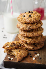 Stack of oatmeal cookies with chocolate on a light background with flakes and a bottle of milk. Selective focus.