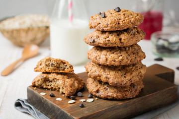 Stack of oatmeal cookies with chocolate on a light background with flakes and a bottle of milk. Selective focus. - obrazy, fototapety, plakaty