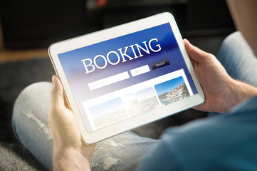Booking app or website on tablet screen. Man searching hotel and flights for holiday and vacation...