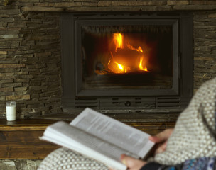 Man reading a book, sitting in a rocking chair with knit plaid in front of a fireplace