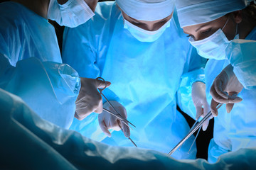 Group of surgeons at work in operating theater toned in blue