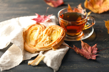 Cup of tea, homemade cookies, autumn maple leaves and woolen scarf on a wooden background.