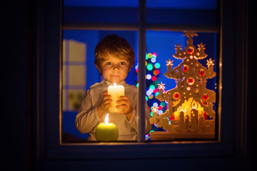 Little kid boy standing by window at Christmas time and holding