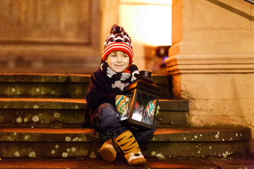 Little cute kid boy with with a light lantern on stairs near church.