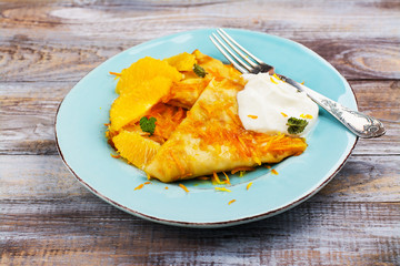 Traditional french dessert crepes suzette with orange syrup and cream on wooden table. Top view. Copy space