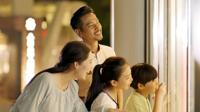 asian family of 4 standing & looking into shop window in slow motion