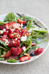 Strawberry blueberry walnut spinach salad topped with a raspberry olive oil vinaigrette dressing and crumbled feta cheese close up shot vertical
