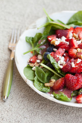 Strawberry blueberry walnut spinach salad topped with a raspberry olive oil vinaigrette dressing and crumbled feta cheese side view
