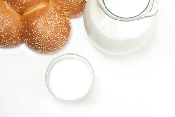 Milk in a glass jug, cup and bun on a white background