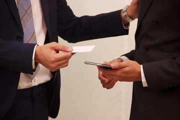 Businessmen exchanging white blank name card, credit card or information on the smart phone. Conceptual Idea of information sharing, communication, connection, paperless, support, partnership