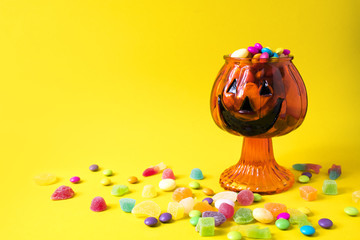 halloween cup pot glass with pumpkin and colorful candy dessert on yellow background