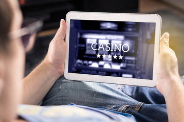 Man playing in an online casino with tablet. Modern gambling application. Slot machine app. Person holding smart mobile device in hand at home. © terovesalainen